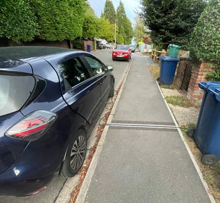A car next to a gully in the pavement outside a house in a street with wheelie bins outside the homes