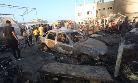 People stand around a burned out car and other charred objects