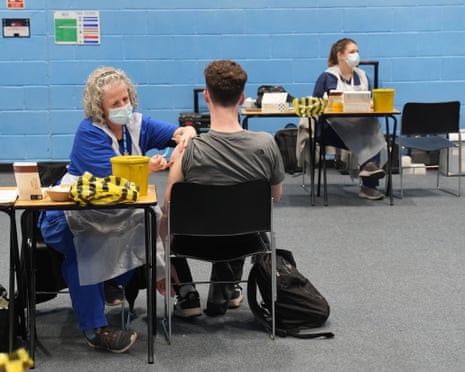 A student receives an injection of a vaccine from a nurse in a university sports hall