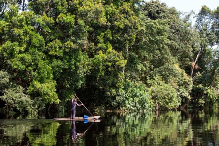 A person stands up paddling a board along a flat stretch of water surrounded by forest.