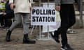 People walk past a polling station sign