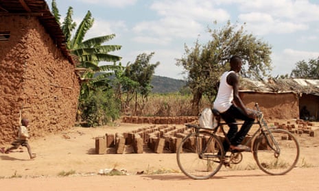 A boy cycles past rows of bricks in Nakivale while a child runs alongside