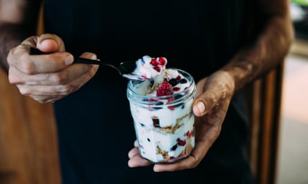 A man holding a jar of dessert made with yoghurt and frozen berry crunch