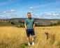 Tom Park-Paul stands with his dog Binks in a golden field near Slaithwaite, hills behind him
