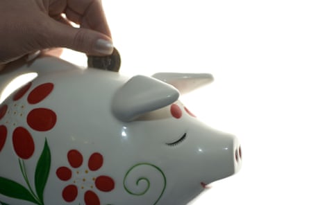 A hand puts a coin in a white piggy bank with red flowers painted on the side