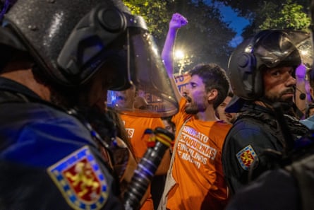 Demonstrator wears orange slogan T.shirt with fist in the air and several police close