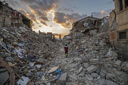 Someone walking through an enormous pile of rubble in what was once a street in the town