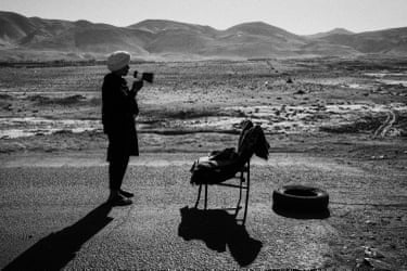 A teenager standing on the roadside holding a m megaphone with a chair in front of him