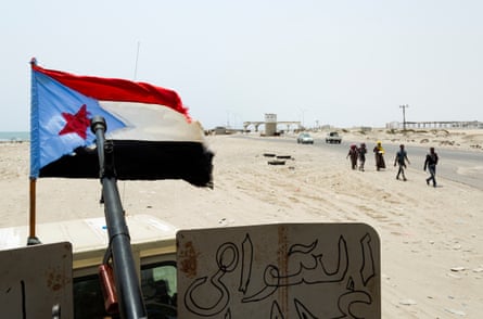 Five people walk through the desert with a South Yemeni flag in the foreground
