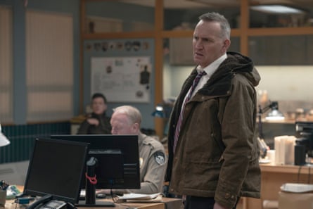 Christopher Eccleston standing in an office beside a police officer on a computer