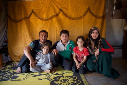 An Arab man sits in a tent next to a woman wearing a headscarf, with two little girls and an older boy between them