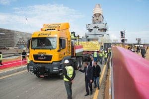 workers look on as a truck hauls a giant statue on a road