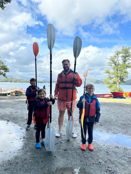A man and three children in life jackets hold paddles for kayaking.
