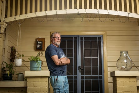 Pete Muskens stands with his arms folded outside his weatherboard house