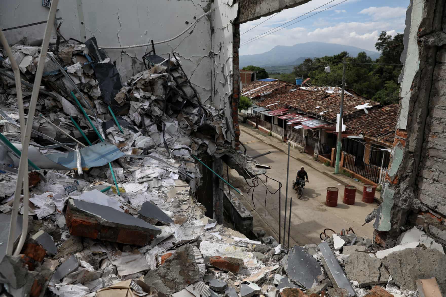 A hole in the wall of a destroyed building shows a bicyclist on a road below