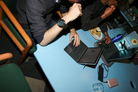 The arms and elbows of several people working at a blue table on laptops, empty plates around them.