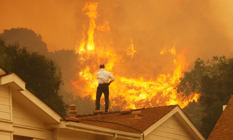 A man on a rooftop looks at approaching flames