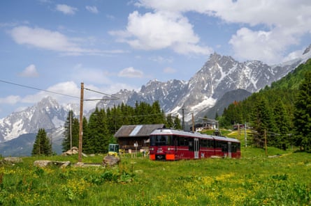 A red tram with meadow in the foreground and mountains and blue sky behind