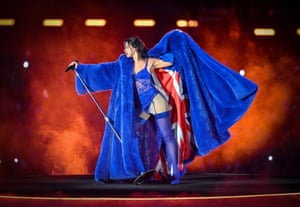 Singer Dua Lipa stands on stage dressed in electric blue with an oversized furry coat lined with the union flag