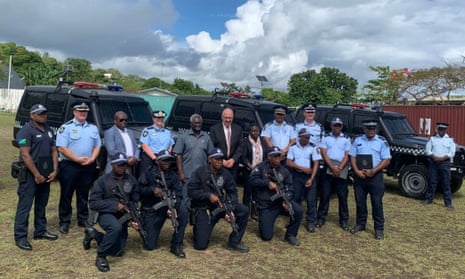 Solomons officers holding rifles kneel in front of officials, with black police four-wheel-drives in background