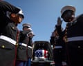 soldiers salute next to a flag draped coffin in a hearse