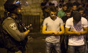 An Israeli border policeman holds a stun grenade in his hand while Palestinian teenagers pray in the street near an entrance to the al Aqsa mosque in Jerusalem.