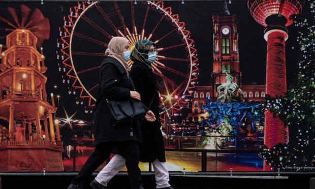 Women wearing face masks walk past the site of a traditional Christmas market at Berlin's Alexanderplatz