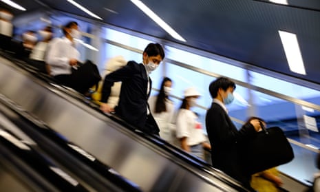 People wearing face masks ride an escalator at a train station in the Shinbashi area of Tokyo on 18 June 2020.