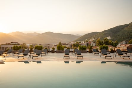 An empty outdoor swimming pool with sunbeds on one side and mountains on the horizon
