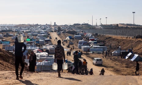 People ferry water at a makeshift tent camp for displaced Palestinians in Rafah near the border with Egypt in the southern Gaza Strip, on 24 January.