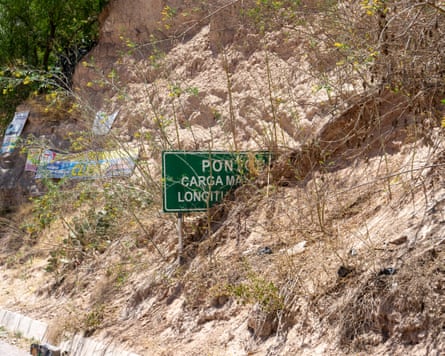 A partly visible green road sign emerges from a steep bank on mud next to a road.