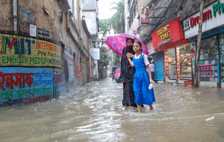 A girl in school uniform with an adult walking through shin-high water.