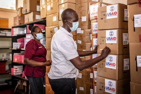 A worker person writes on a stack of boxes labelled 'USAID'