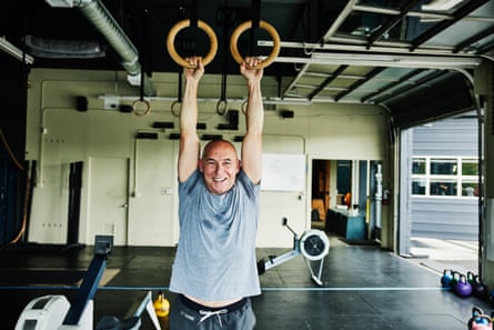 Smiling mature man doing pull-ups on rings in gym.