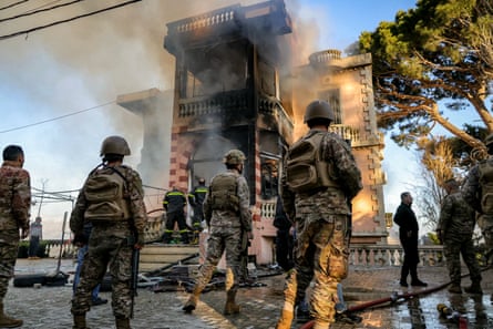 Soldiers look at building emitting smoke from bombardment.
