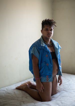 Trans man kneels on a bed