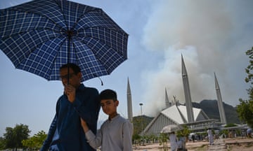 A man and boy walk way from a mosque carrying an umbrella to protect them from the heat.