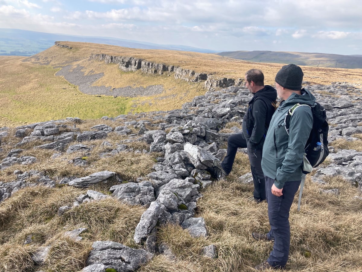 Two men in walking clothes look out across an escarpment on a fine day