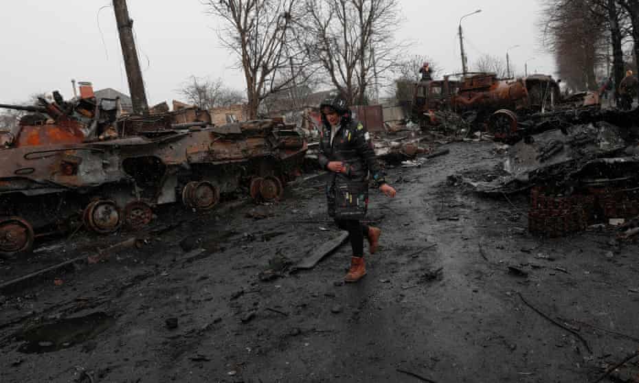 A Ukrainian woman walks pass destroyed Russian military vehicles in the city of Bucha