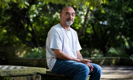 Midshot of Andrew Malkinson looking at the camera sat outside against a backdrop of tree foliage.