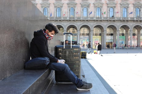 A tourist wears a protective mask and gloves as he sits with his luggage in the Duomo Square on Friday in Milan.
