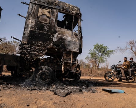 A motorcyclist rides past a burnt truck