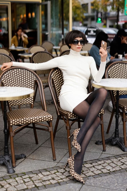 Model poses at street cafe table in white dress and sheer black tights