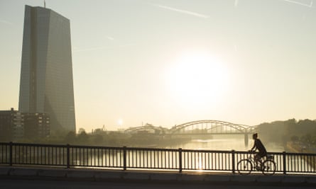 A cyclist rides across a bridge as the skyscraper headquarters of the European Central Bank.