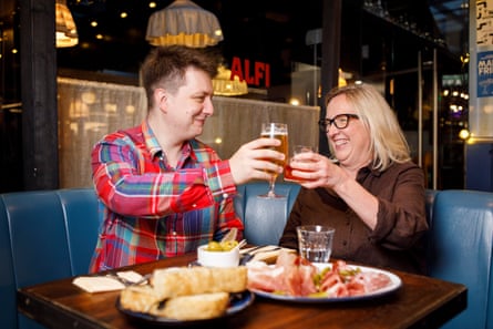Ted and Nicky clinking glasses at a restaurant table