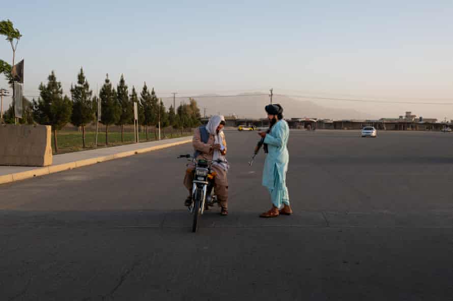 A Taliban policeman with a gun checks a motorcyclist’s papers at a checkpoint in Kandahar