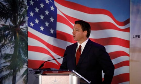 Ron DeSantis in front of a cardboard cutout American flag and palm trees.