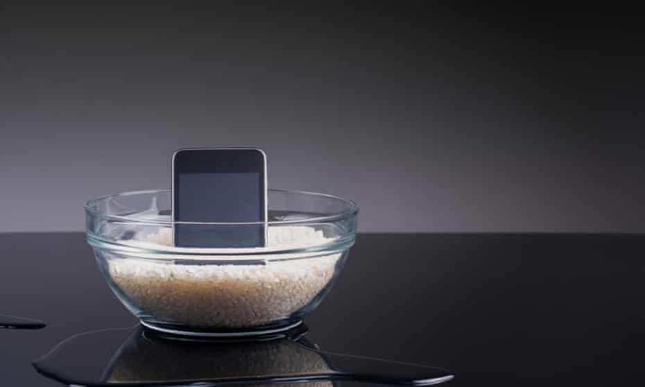 Drying rice<br>A conceptual image with a phone inside a bowl with rice and reflected on black, there is also some water on the floor.