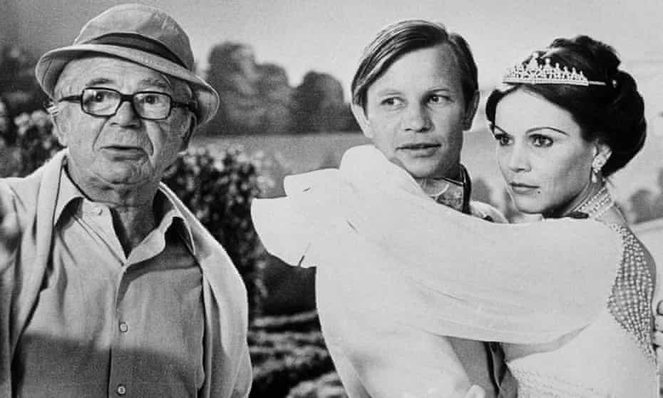 1978 photo of Billy Wilder in a hat next to Michael York, being hugged by Marthe Keller in a tiara