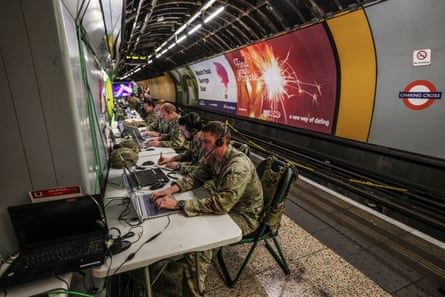 A row of soldiers working on desks set up along a disused London Underground platform